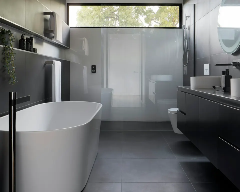 Renovated bathroom with dark large-format tiles, glass shower screen and freestanding bath