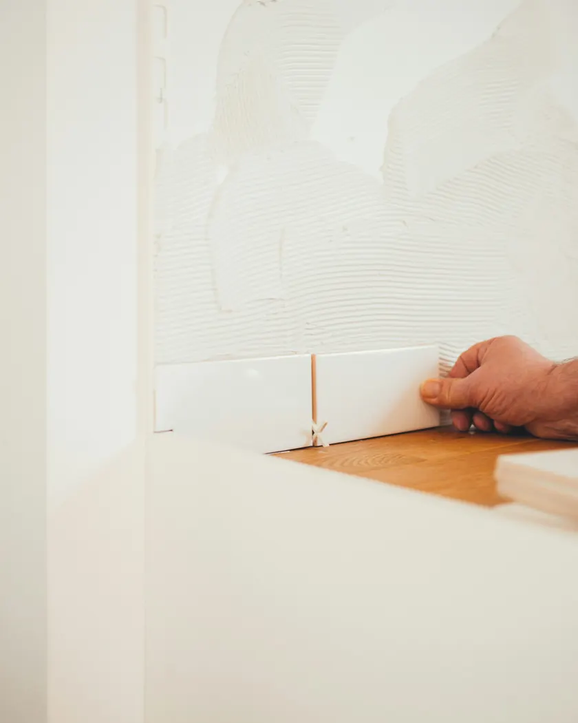 Tiler setting a wall tile on notched adhesive with spacers for even joints